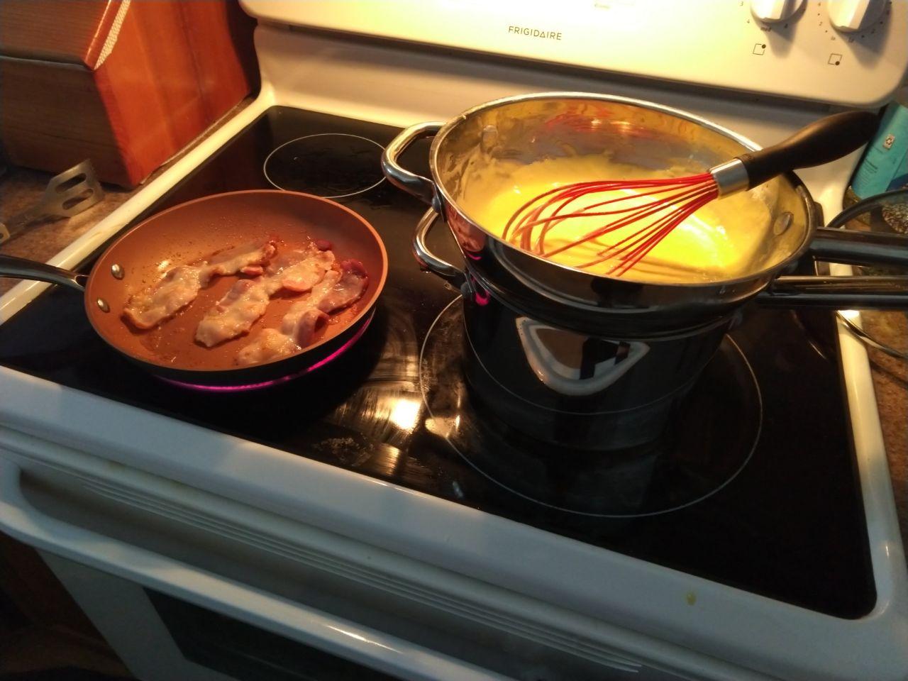 Hollandaise cooking in double boiler with bacon frying in a pan. Hollandaise cooking in double boiler with bacon frying in a pan.