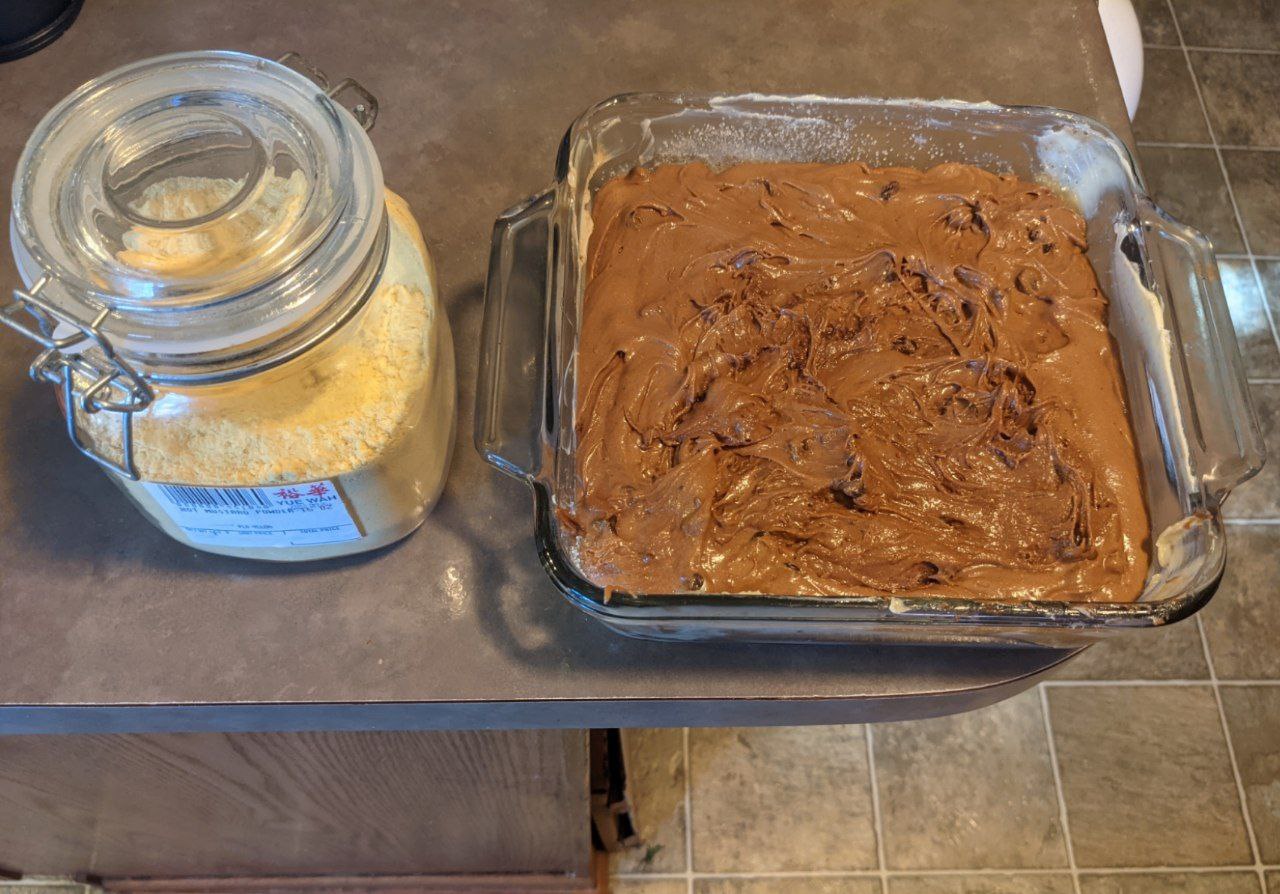 Pan of mustard brownie batter next to jar of mustard powder. Pan of mustard brownie batter next to jar of mustard powder.