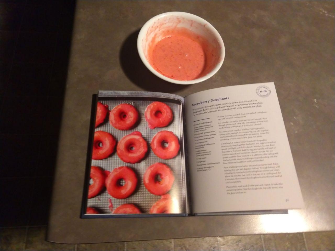 Strawberry donut glaze next to cookbook. Strawberry donut glaze next to cookbook.