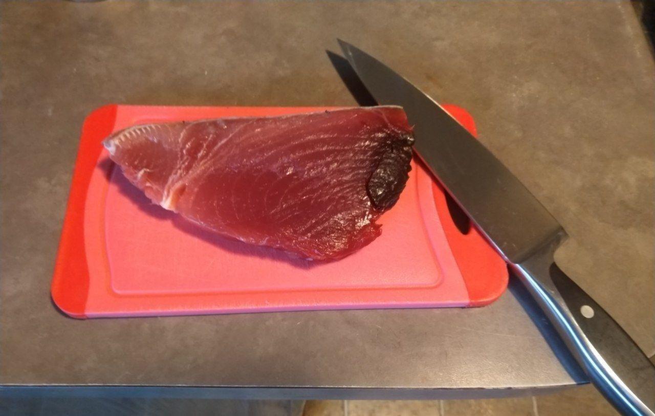 Raw tuna steak on a cutting board with a knife. Raw tuna steak on a cutting board with a knife.
