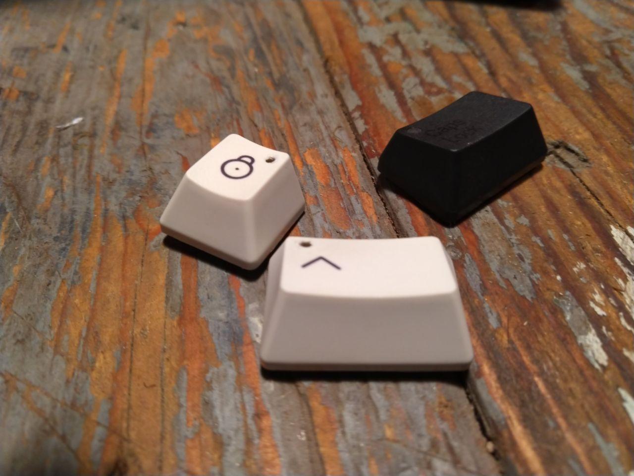 Keycaps with holes drilled through, next to the stock black keycap.