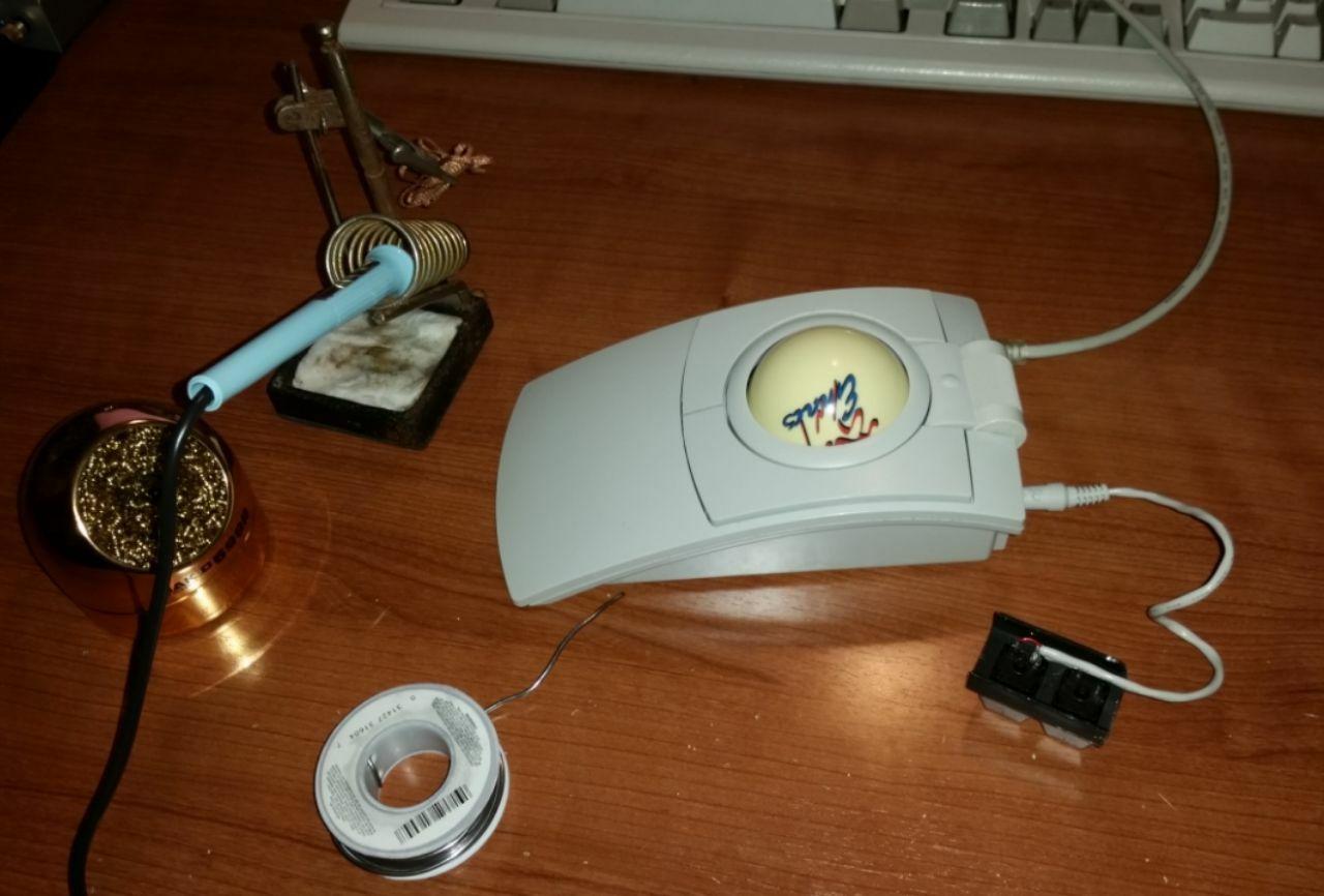 Half built switch casing connected to trackball next to a soldering iron.